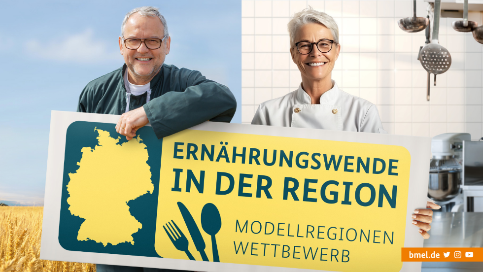 Zwei Personen halten ein Schild mit der Aufschrift "Modellregionenwettbewerb - Ernährungswende in der Region". Es zeigt die Vernetzung zwischen Landwirtschaft und Großküchen.